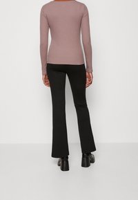 Långärmad ribbad topp i mauve tillsammans med svarta utsvängda byxor, med en slät yta och åtsittande design. Svarta klumpiga klackskor.