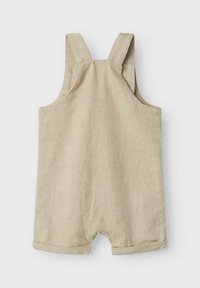 Mono de lino beige con tirantes anchos y puños enrollados. Presenta cierres a presión en los hombros para facilitar el vestido.