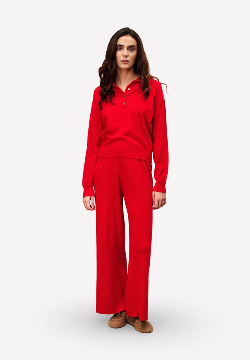 Rode gebreide trui met een hoge hals en korte knopen, gecombineerd met rode broek met wijde pijpen. Zachte textuur, ontspannen pasvorm, minimalistisch ontwerp.