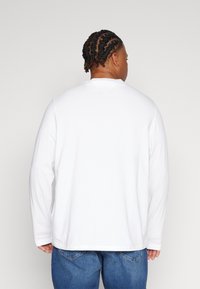 Hvit skjorte med lange ermer og rund hals, laget av mykt stoff. Bakside som viser en avslappet passform og en rett kant, kombinert med blå jeans.