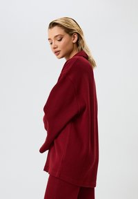 Maglia in burgundy a coste, oversize, con un fit rilassato e maniche morbide, caratterizzata da un collo rotondo e una texture morbida.