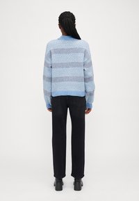 Pull en maille bleu clair avec un motif texturé, à rayures horizontales. Assorti à un jean noir et des bottes à talons larges.