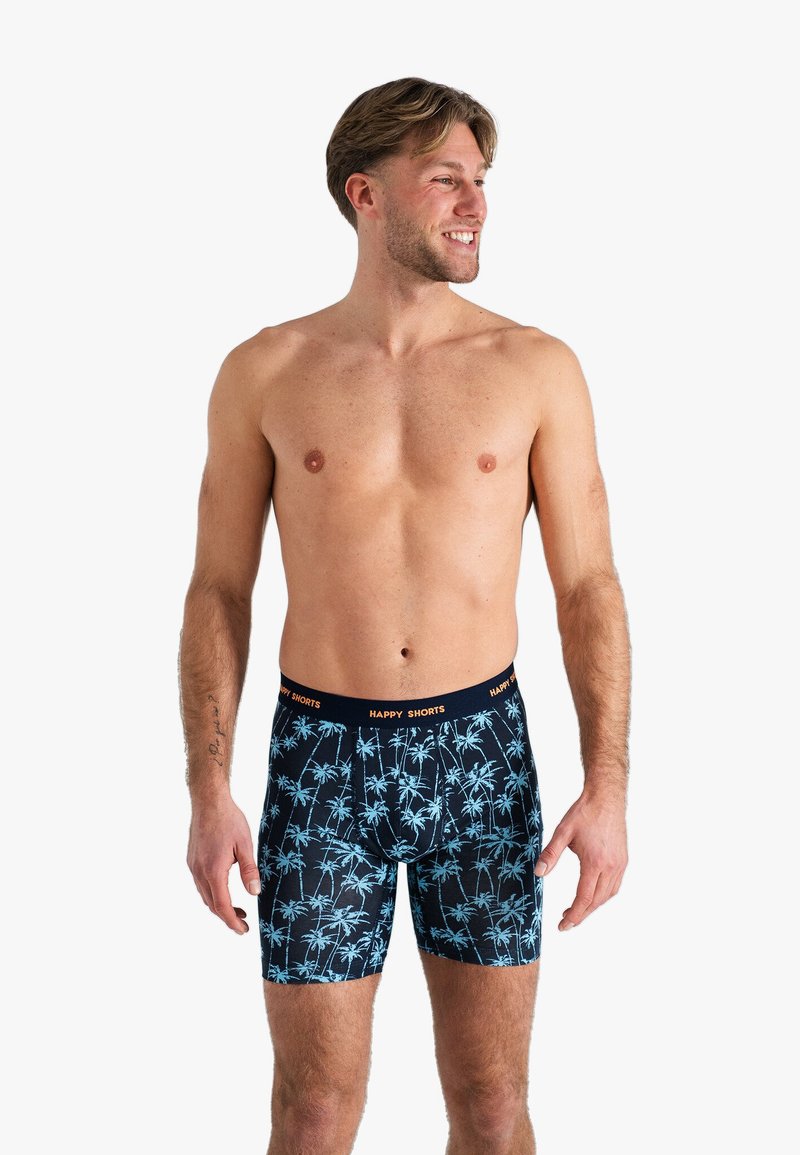 Mannen onderbroeken in marineblauw met een lichtblauw palmboom patroon. Voorzien van een elastische tailleband met "HAPPY SHORTS" in oranje tekst.