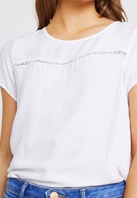 Weißes kurzärmliges Blusenshirt mit einem strukturierten Spitzenpanel über der Brust, aus einem leichten Stoff mit lässigem Schnitt.