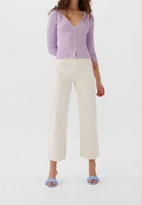 Světlofialový žebrovaný cardigan s knoflíky, doplněný krémovými širokými kalhotami s vysokým pasem a modrými pletenými nazouvacími sandály.