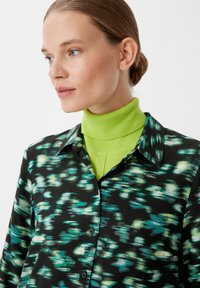 Black blouse with a vibrant green and blue abstract pattern, featuring a button-up front, collar, and layered over a bright green turtleneck.