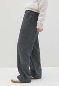 Pantaloni larghi grigi e testurizzati con vita alta, dotati di pieghe frontali e una vestibilità rilassata, abbinati a sneakers bianche.