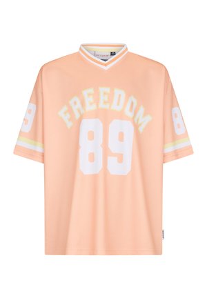 Brzoskwiniowa koszulka sportowa z białym numerem 89 z przodu i na rękawach, napis "FREEDOM" nad numerem z przodu oraz biały kołnierz w kształcie litery V z paskami.