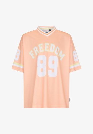 Perzikkleurig sportshirt met wit nummer 89 op de voorkant en mouwen, "FREEDOM" tekst boven het voorkantnummer, en witte gestreepte V-hals