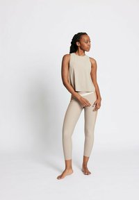 Beige Activewear-Set mit ärmellosem Oberteil und hochgeschnittenen Leggings. Der Stoff hat eine glatte Textur und eine figurbetonte Passform.
