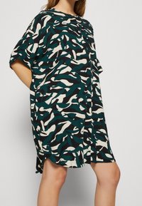 Sukienka z krótkim rękawem w jedwabnym materiale, z abstrakcyjnym wzorem w kolorach zielonym, białym i czarnym, z okrągłym dekoltem i luźnym krojem.