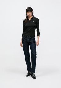 Polo a maniche lunghe nere con colletto, abbinata a jeans blu scuro a gamba dritta e stivaletti neri alla caviglia. Design semplice e aderente.