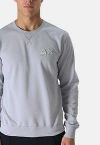 Felpa grigia chiara con polsini a costine, scollo rotondo e logo ricamato discreto sul petto. Tessuto dalla superficie liscia, design minimale.