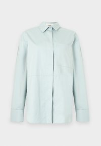 Camisa de manga larga azul claro con botones, cuello puntiagudo y bolsillo en el pecho izquierdo, mostrada sobre un fondo blanco sencillo.