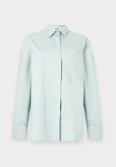 Ανοιχτό μπλε πουκάμισο με μακριά μανίκια, μπουτόν, μυτερό γιακά και αριστερή τσέπη στο στήθος, παρουσιάζεται σε απλό λευκό φόντο.