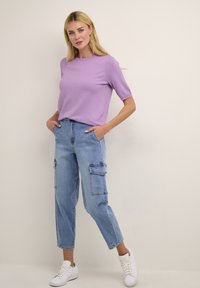 Top corto viola chiaro a maniche corte abbinato a jeans cargo blu chiaro con numerose tasche, completato da sneakers bianche. Look semplice e informale.