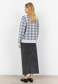 Svetr s šedým houndstooth vzorem a dlouhými rukávy, kombinovaný s tmavě šedou maxi kordovou sukní a černými plochými botami.