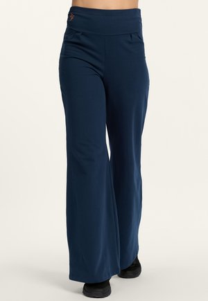 Marineblaue, weit geschnittene Hose mit hohem Bund, getragen mit schwarzen Schuhen, gezeigt von der Taille bis zu den Füßen vor neutralem Hintergrund.