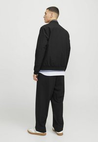 Fekete bomberdzseki ribbed gallérral, fekete bő, laza nadrág és fehér sneakers, barna talppal. Minimális dizájn, látható minták nélkül.