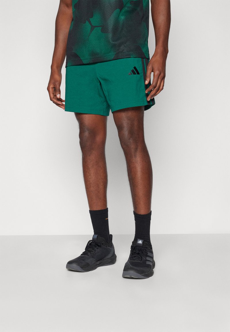 Grønne treningshorts med elastisk midjebånd, brukt med svarte sokker og svarte joggesko. Skjorten har et mørkegrønt bladmønster.