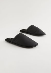 Chaussons noirs à enfiler avec une tige en tissu texturé à rainures et un intérieur doux et moelleux. Bout rond et semelle en caoutchouc plate. Sans ornement.