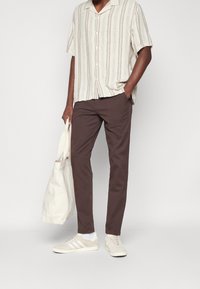 Kortärmad randig skjorta i ljusbeige med blå ränder, bruna byxor, beige sneakers och en krämfärgad tote-väska.