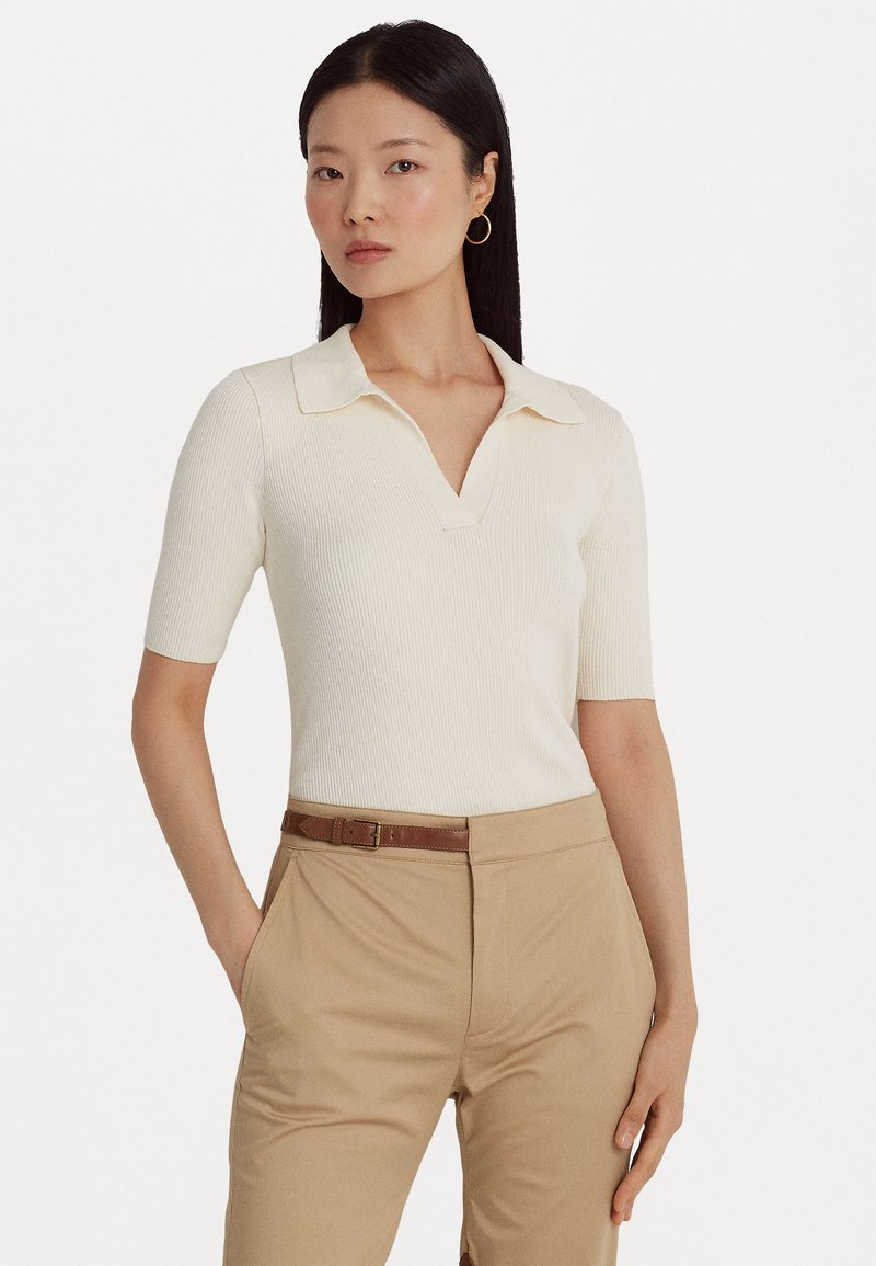 Ribbed cream polo toppi V-kauluksella ja lyhyillä hihoilla, yhdistettynä beigeihin housuihin ja ruskeaan vyöhön. Sujuva pinta ja tiukkamuotoinen muotoilu.