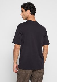 Zwart katoenen T-shirt met korte mouwen en een ronde hals. Soepele textuur en ontspannen pasvorm. Zichtbare stiksel-details.