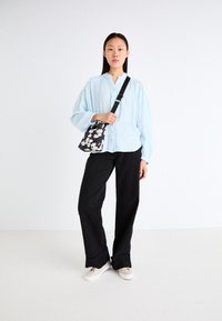 Cămașă albastră deschis, cu un finisaj texturat, asociată cu pantaloni negri cu croială largă și o geantă de umăr cu un model floral.