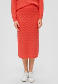 Brede gebreide midi-rok in koraal met een zigzagpatroon, een zachte textuur en een ribbelzoom, gecombineerd met witte sneakers.