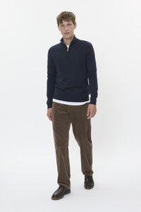 Navy zip-up sweater with long sleeves, layered over a white shirt. Paired with brown corduroy pants and dark shoes, creating a casual look.