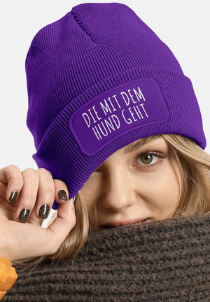 Purple knit beanie with a rectangular patch displaying the text "DIE MIT DEM HUND GEHT" in white. Ribbed texture and snug fit.
