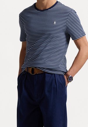 Uomo che indossa una t-shirt a righe blu navy e bianca a maniche corte, pantaloni blu navy, cintura in pelle marrone e orologio da polso con quadrante blu e cinturino marrone.