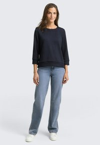 Marineblauwe sweatshirt met textuur en driekwartmouwen, gecombineerd met lichtblauwe rechte jeans en witte sneakers.