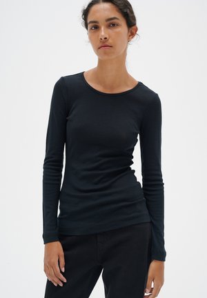 Svart långärmad T-shirt med rund halsringning, figursydd design och mjuk textur, kombinerad med mörka byxor. Inga mönster eller dekorationer.