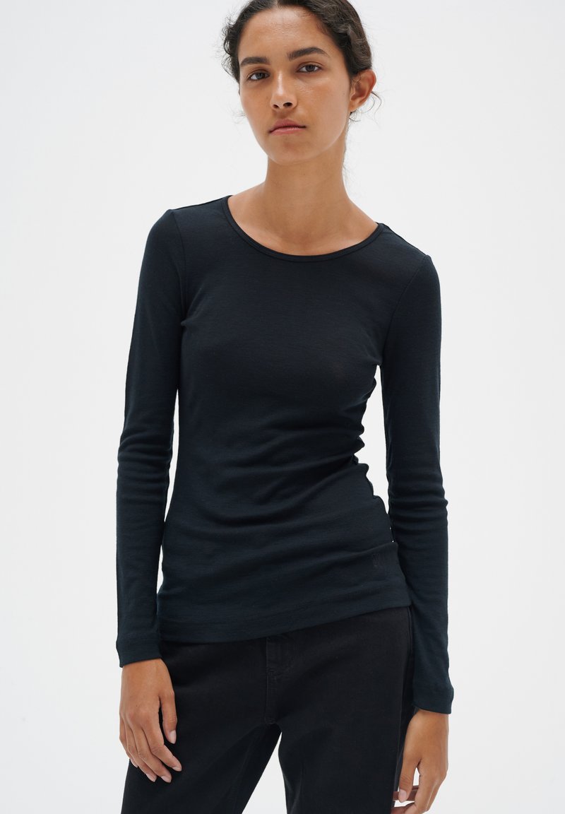 Svart långärmad T-shirt med rund halsringning, figursydd design och mjuk textur, kombinerad med mörka byxor. Inga mönster eller dekorationer.