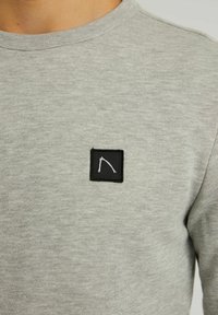 Felpa grigia con collo rotondo, tessuto testurizzato e toppa rettangolare nera con disegno bianco sul lato sinistro del petto.