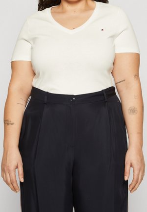 Top blanco de manga corta en forma de V combinado con pantalones negros de cintura alta con cierre de cremallera y botón, rayas laterales y una textura suave.