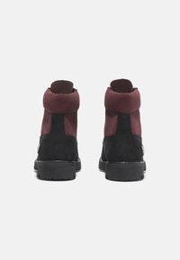 Bottes en suede jusqu'à la cheville avec un empeigne bordeaux et une partie inférieure noire, dotées d'un col rembourré et d'une semelle en caoutchouc robuste pour une meilleure traction.