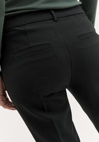Czarne spersonalizowane spodnie o slim fit, z dwiema kieszeniami z tyłu, gładką fakturą i średnim stanem pasa.