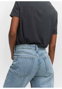 Jean taille haute bleu clair avec une finition délavée, comprenant des poches arrière et une fermeture à bouton, associé à un t-shirt gris foncé à manches courtes.