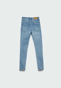 Jeans de mezclilla azul claro con un diseño ajustado, cinco bolsillos y una etiqueta de cuero marrón en la cinturilla en la parte posterior. Textura suave, sin patrones prominentes.