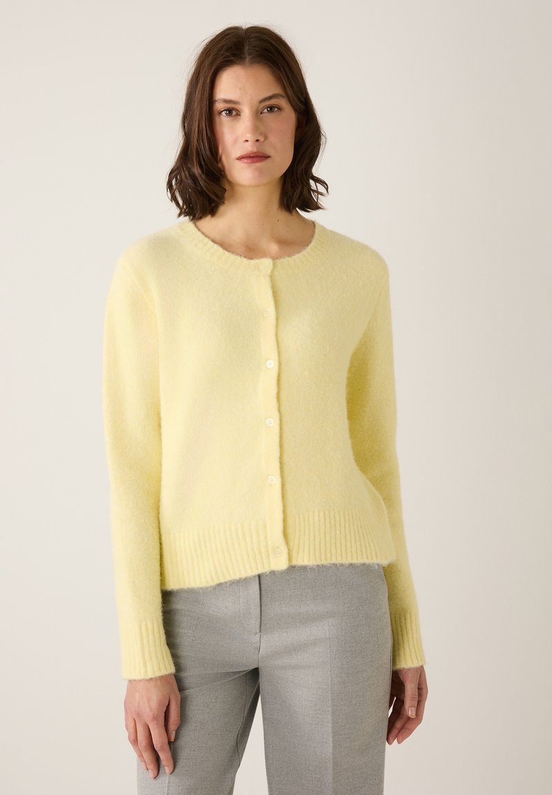 Hellgelber Pullover aus weichem, flauschigem Material, mit rundem Ausschnitt, Knopfleiste sowie geripptem Saum und Bündchen.