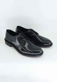 Scarpe da uomo in pelle nera con superficie lucida, punta tonda e design con lacci. Presentano una suola cucita in contrasto e tacco basso.
