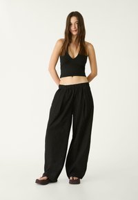 Schwarzes Cropped-Top mit V-Ausschnitt, kombiniert mit lockeren schwarzen Hosen mit elastischem Bund und weitem Bein.