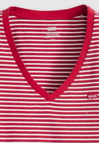 Punane ja valge triibuline V-kaelusega T-särk, mis on valmistatud puuvillast. Omab soonikserva kaelust ja väikest Levi'si logo sildit paremal all.