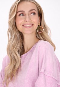 Felpa oversize rosa chiaro con finitura testurizzata, caratterizzata da un collo rotondo e spalle scese. Orecchini a cerchio colorati accentuano il look.