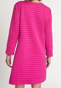 Fuchsiové šaty s texturovaným, prošívaným vzorem, dlouhými rukávy a kulatým výstřihem; polodlouhý design poskytuje jednoduchou siluetu.