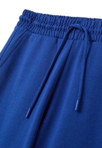 Blauwe stretchstof joggers met een elastische tailleband en een trekkoord. Zachte textuur met zichtbare stikdetails.