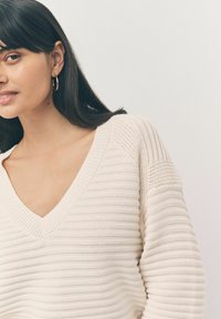 Maglione lavorato a maglia color crema con scollo a V, caratterizzato da motivi a coste orizzontali e maniche morbide. Texture soffice e design leggero.